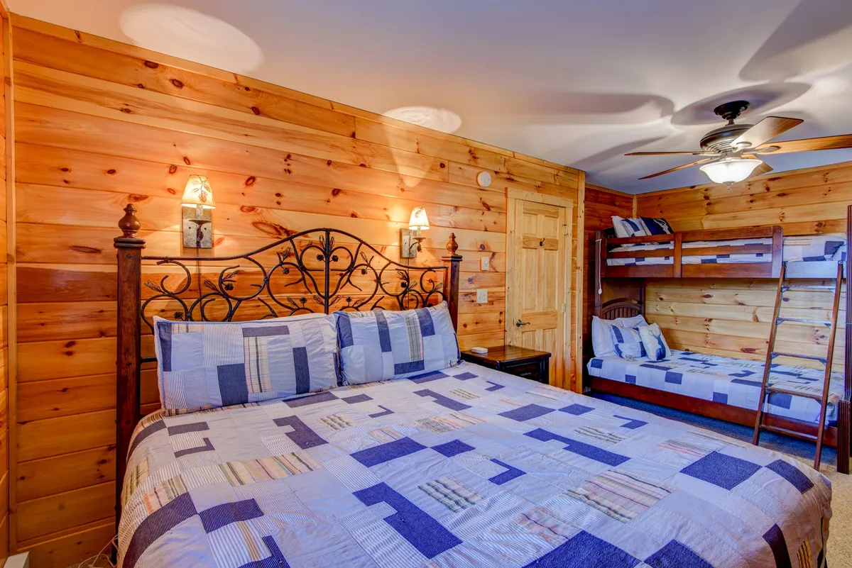 This image features a bedroom with a main bed (quilted cover) and a bunk bed set against wood paneling. Warm lighting and inviting decor create a family-friendly, flexible sleeping space, ideal for mixed-age groups.