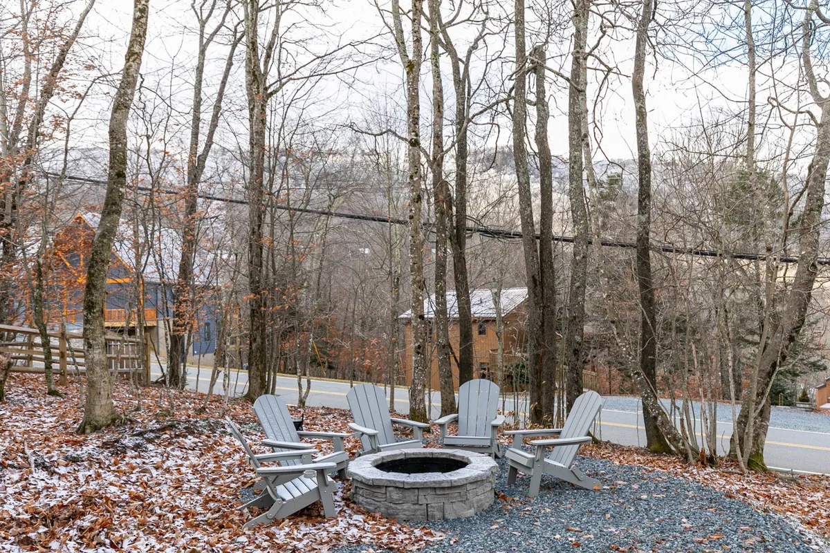 An inviting fire pit area with Adirondack chairs arranged in a circle, surrounded by trees. The cozy setup evokes evenings of storytelling, marshmallow roasting, and stargazing under the mountain sky.