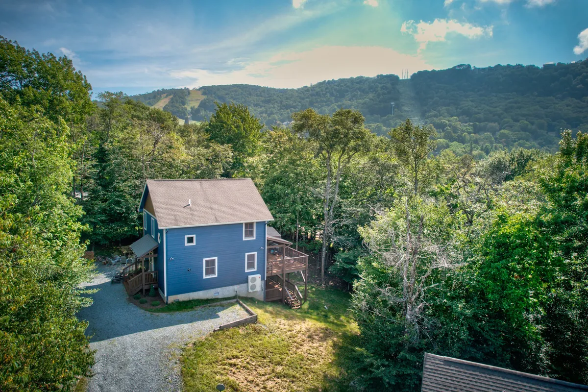 This exterior shot highlights the blue house nestled among trees, with the deck area visible. It's a peaceful woodland setting that suggests easy access to outdoor activities and wildlife watching, while also evoking a sense of retreat after a day of adventure.