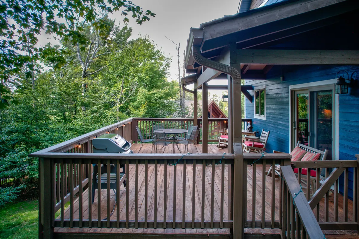 This image shows a spacious wooden deck with a grill and outdoor seating nestled amidst lush greenery. The area invites guests to enjoy al fresco dining, morning coffee, and leisurely relaxation while soaking in the natural surroundings. The positioning of the grill and table make it ideal for gatherings and meals outdoors.