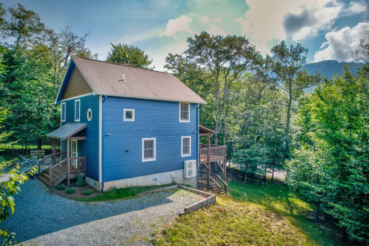A welcoming exterior shot of the blue house with its deck area, surrounded by vibrant greenery. The image highlights the inviting outdoor gathering space and its integration with the surrounding natural environment.