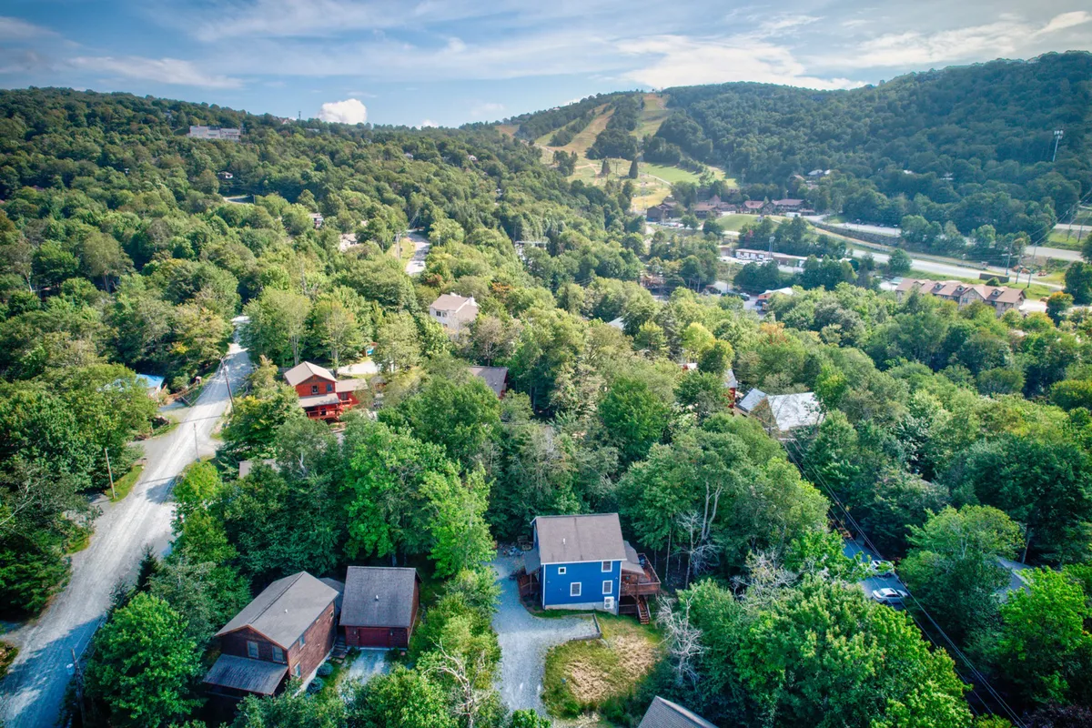 A sweeping view over rolling hills dotted with wooded areas, winding roads, and scattered homes—showcasing the broader High Country landscape. The scene hints at the possibilities for hiking, biking, fall foliage tours, and skiing, set in a tranquil mountain environment.