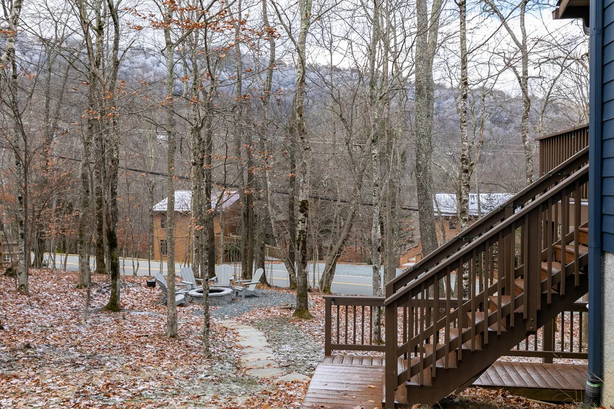 An exterior view showing wooden stairs leading down a pathway, flanked by bare trees and opening up to a mountain view in the distance. The setting is peaceful and naturally wild, suggesting immediate access to nature and nearby hiking trails.