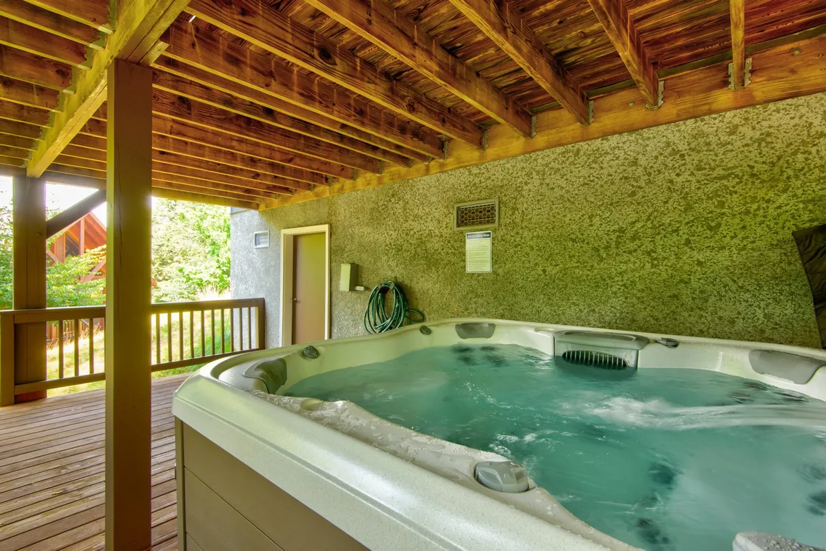 A tranquil hot tub set under a wooden ceiling with a view of a deck railing and the outdoors. The space is perfect for immersive relaxation, with sunset or nature views.